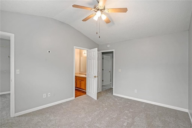 unfurnished bedroom with ceiling fan, a walk in closet, a closet, light carpet, and vaulted ceiling