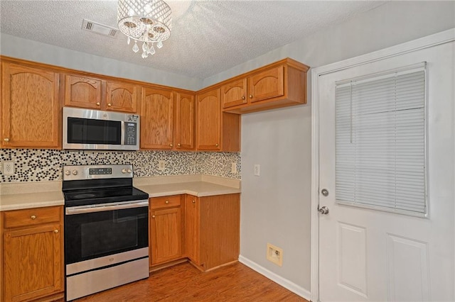 kitchen with a notable chandelier, appliances with stainless steel finishes, light wood-type flooring, and decorative backsplash