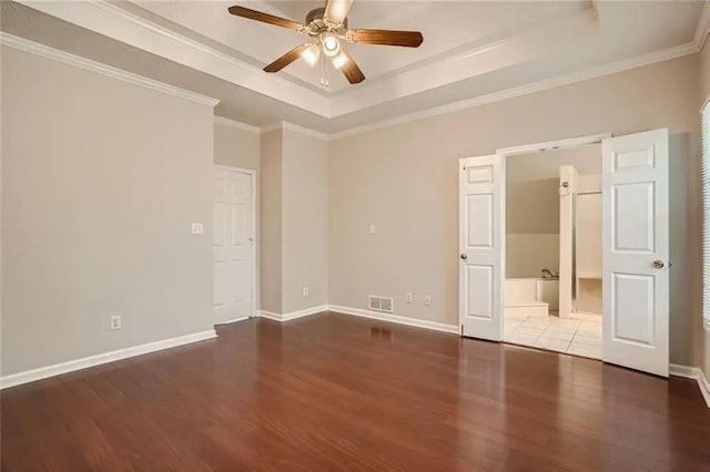 unfurnished bedroom featuring ceiling fan, ensuite bathroom, hardwood / wood-style floors, a tray ceiling, and ornamental molding