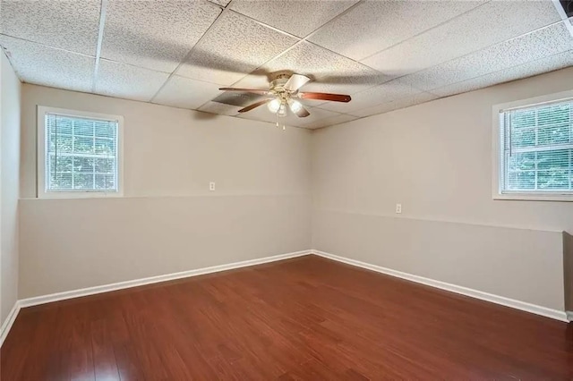 unfurnished room featuring dark hardwood / wood-style flooring, a drop ceiling, a healthy amount of sunlight, and ceiling fan