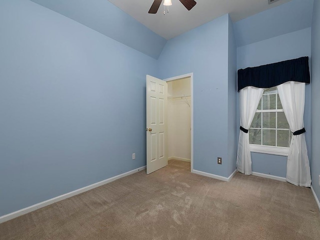 unfurnished bedroom featuring carpet, a walk in closet, baseboards, a ceiling fan, and lofted ceiling