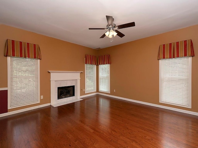 unfurnished living room featuring a ceiling fan, a tiled fireplace, wood finished floors, and baseboards