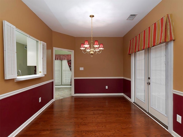 unfurnished dining area with an inviting chandelier, wood finished floors, visible vents, and baseboards
