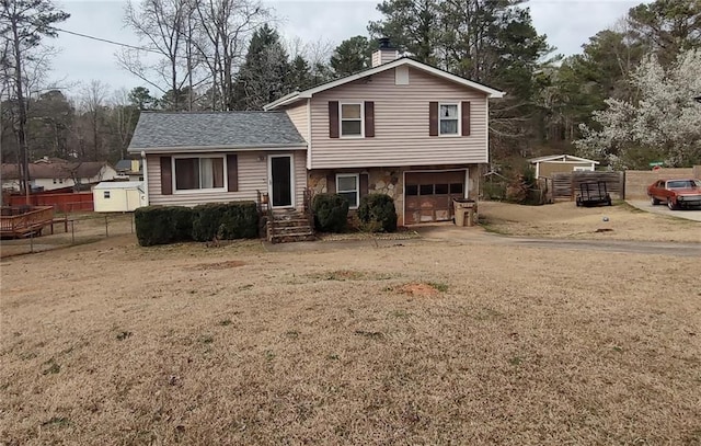 tri-level home with fence, driveway, an attached garage, a chimney, and stone siding