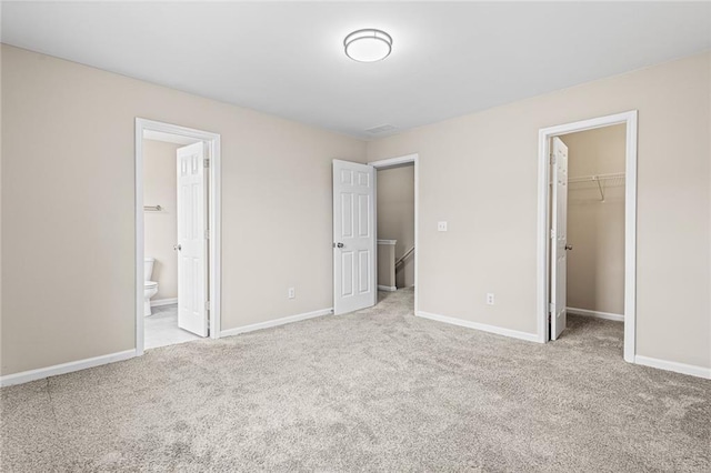 unfurnished bedroom with light carpet, a closet, a spacious closet, and ensuite bath