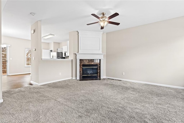 unfurnished living room with ceiling fan, carpet floors, and a premium fireplace