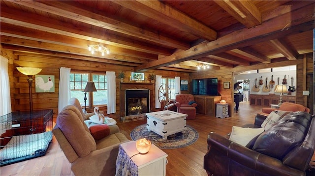 living room with wood walls, beam ceiling, a fireplace with raised hearth, and hardwood / wood-style floors