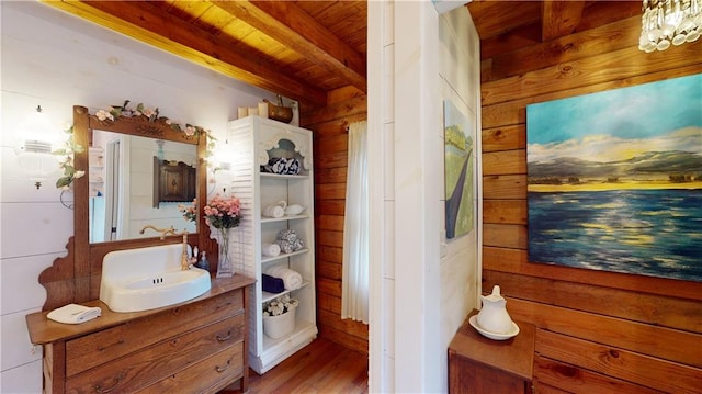 bathroom with beam ceiling, wooden walls, vanity, wood finished floors, and wooden ceiling