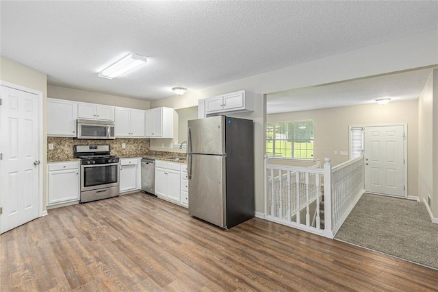 7420 Bristol Cir, Douglasville, GA 30134 - kitchen featuring appliances with stainless steel finishes, white cabinets, wood finished floors, decorative backsplash, and a textured ceiling