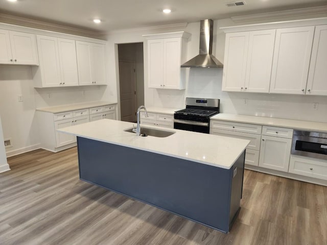 kitchen featuring stainless steel appliances, sink, wall chimney range hood, a center island with sink, and white cabinetry