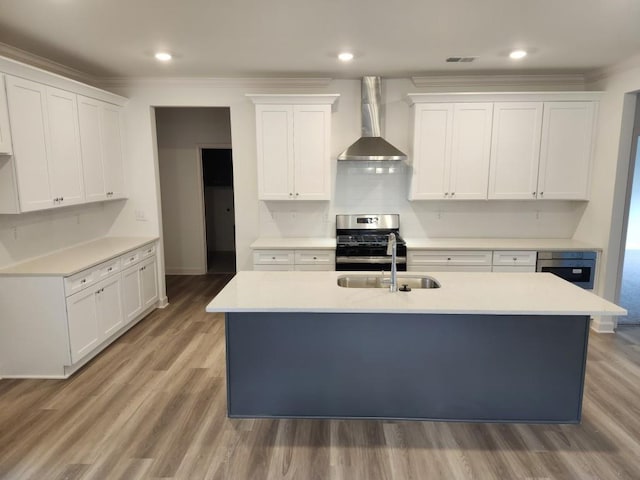 kitchen with white cabinetry, sink, wall chimney range hood, hardwood / wood-style floors, and an island with sink