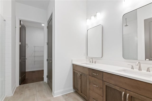 bathroom with a tile shower, double vanity, a spacious closet, and a sink