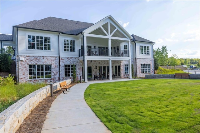 back of property featuring a balcony, a yard, stone siding, roof with shingles, and a patio area