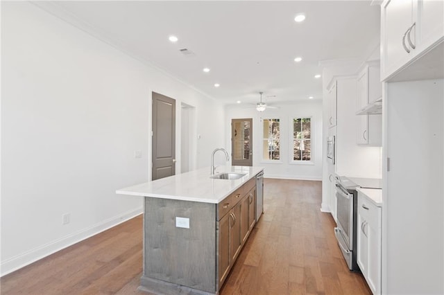 kitchen with appliances with stainless steel finishes, a sink, a kitchen island with sink, and light wood-style floors