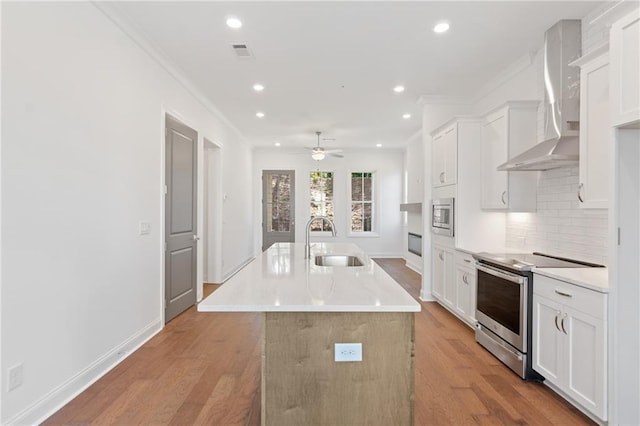 kitchen with visible vents, a kitchen island with sink, stainless steel appliances, wall chimney range hood, and a sink