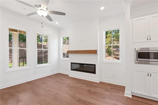 unfurnished living room featuring baseboards, a glass covered fireplace, ornamental molding, wood finished floors, and recessed lighting