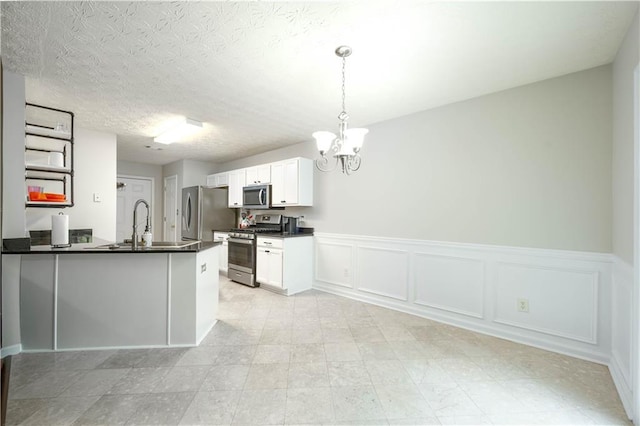 5279 Leecroft Dr, Buford, GA 30518 - kitchen with stainless steel appliances, dark countertops, a chandelier, wainscoting, and white cabinets