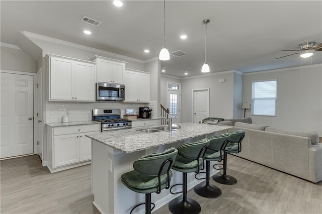 kitchen with decorative light fixtures, white cabinetry, a breakfast bar area, stainless steel appliances, and a center island with sink