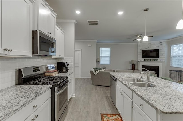 kitchen with sink, a large fireplace, ornamental molding, stainless steel appliances, and white cabinets