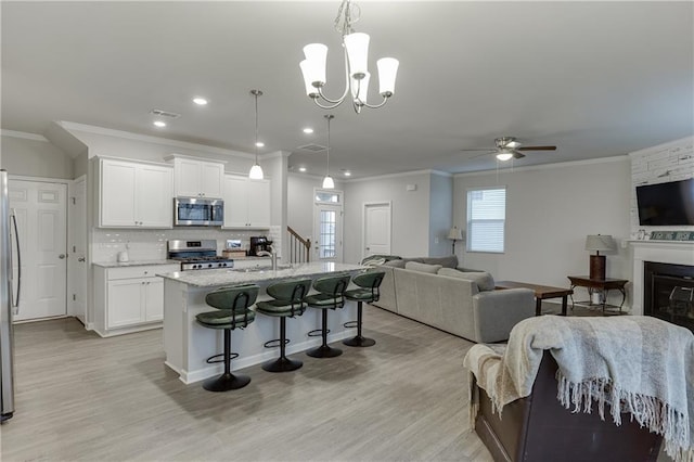 kitchen featuring a kitchen island with sink, stainless steel appliances, a kitchen breakfast bar, white cabinets, and decorative light fixtures