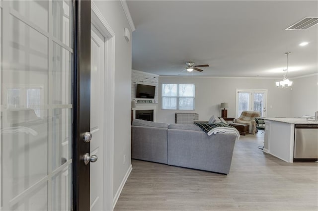 living room with crown molding, a fireplace, light wood finished floors, visible vents, and ceiling fan with notable chandelier