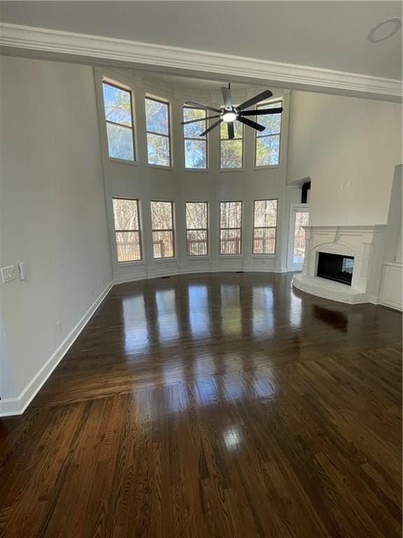 unfurnished living room featuring dark wood-style floors, a ceiling fan, baseboards, ornamental molding, and a glass covered fireplace