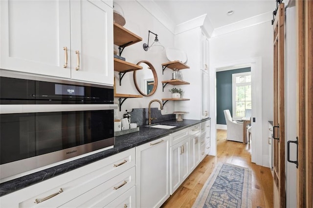 kitchen featuring open shelves, light wood-type flooring, a barn door, a sink, and white cabinetry