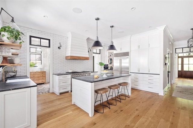 kitchen with high quality appliances, open shelves, light wood-type flooring, a sink, and premium range hood