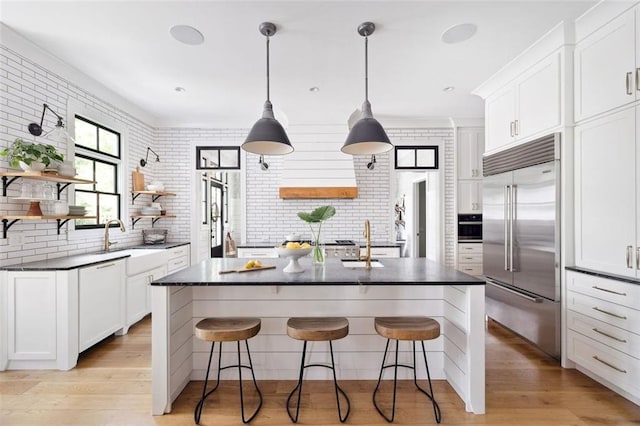 kitchen with open shelves, a kitchen breakfast bar, built in fridge, a sink, and light wood finished floors
