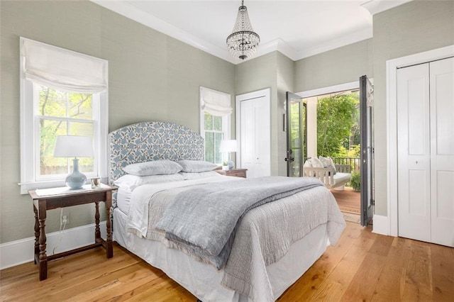 bedroom featuring access to exterior, light wood-type flooring, a notable chandelier, multiple closets, and ornamental molding