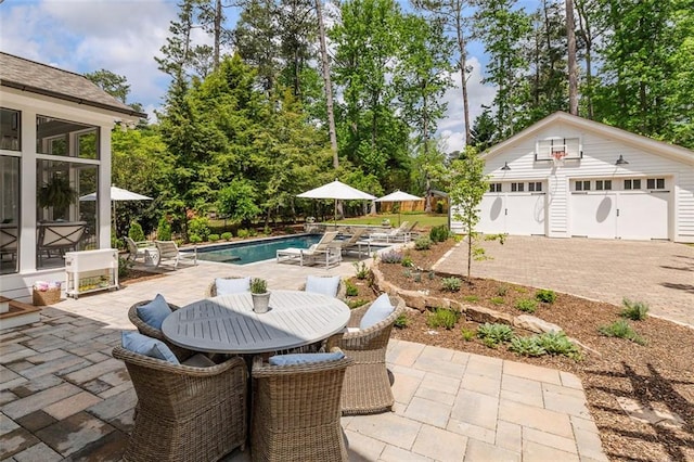 view of patio / terrace with a detached garage, outdoor dining space, an outbuilding, and an outdoor pool
