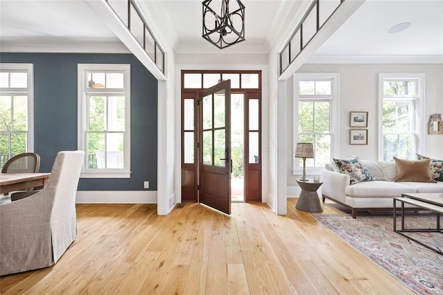 foyer entrance featuring an inviting chandelier, ornamental molding, light wood-style flooring, and baseboards