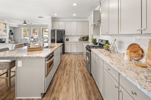 kitchen with dark hardwood / wood-style floors, an island with sink, a kitchen bar, light stone counters, and stainless steel appliances