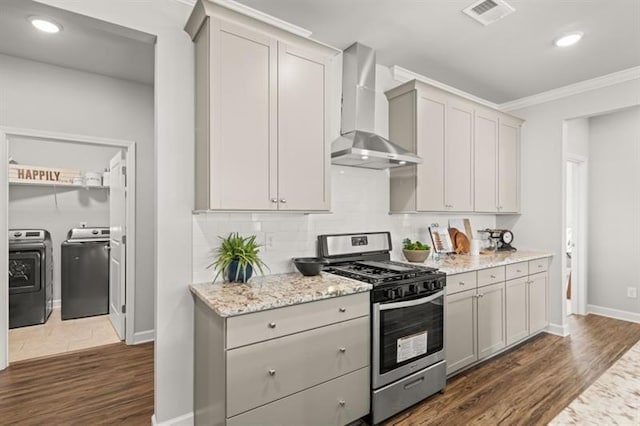 kitchen with dark hardwood / wood-style floors, gray cabinetry, washing machine and clothes dryer, gas range, and wall chimney exhaust hood