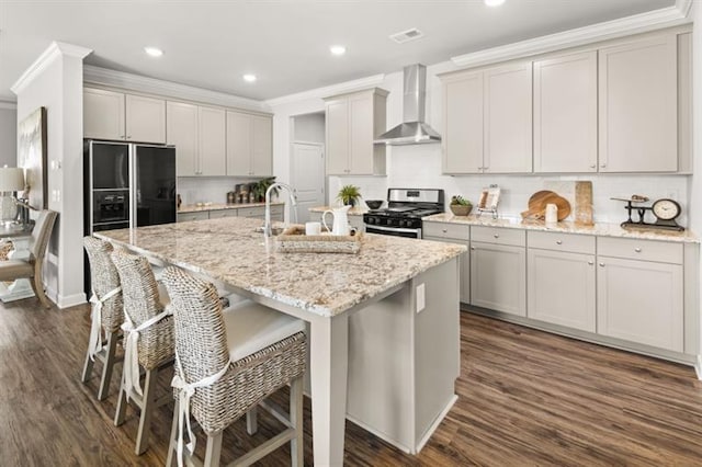 kitchen featuring wall chimney range hood, stainless steel gas range, a kitchen island with sink, dark hardwood / wood-style flooring, and black fridge with ice dispenser