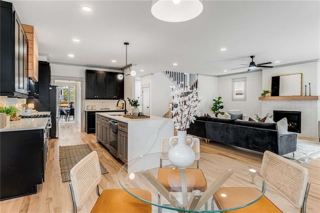 kitchen featuring light countertops, backsplash, a glass covered fireplace, dark cabinetry, and dishwasher