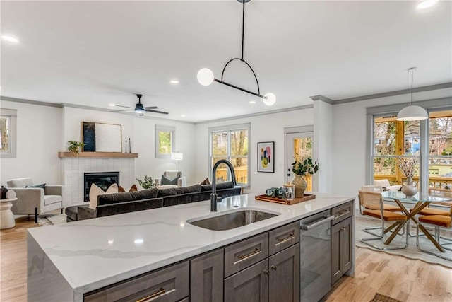 kitchen with a sink, light wood-style floors, hanging light fixtures, stainless steel dishwasher, and crown molding