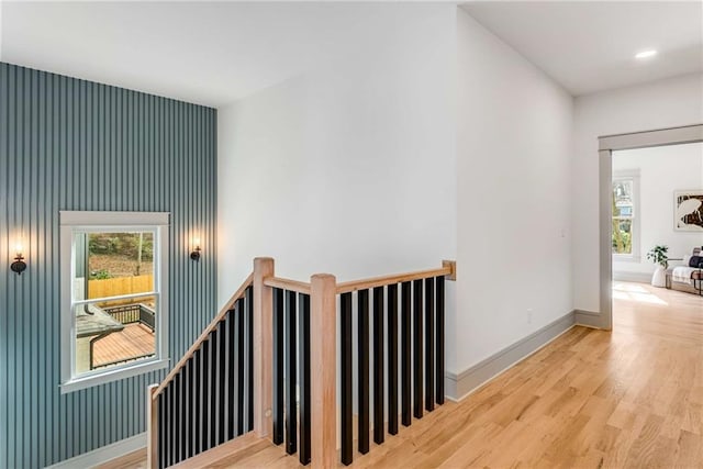 corridor featuring baseboards, wood finished floors, and an upstairs landing