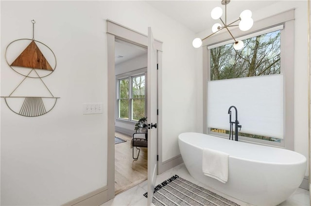 full bathroom with a freestanding bath, marble finish floor, a notable chandelier, and baseboards