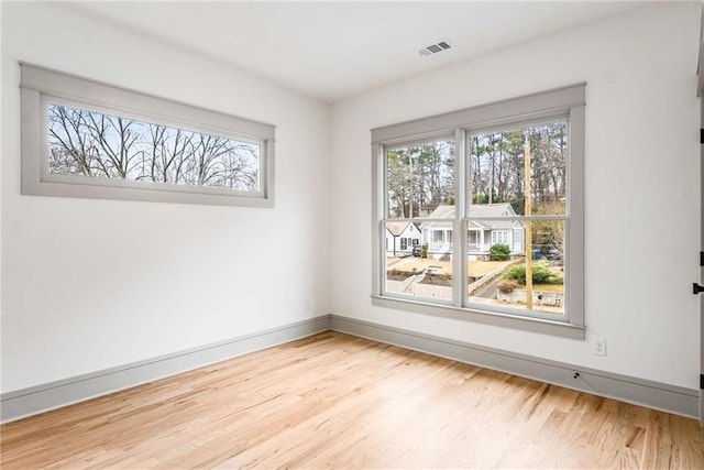 empty room with wood finished floors, visible vents, and baseboards