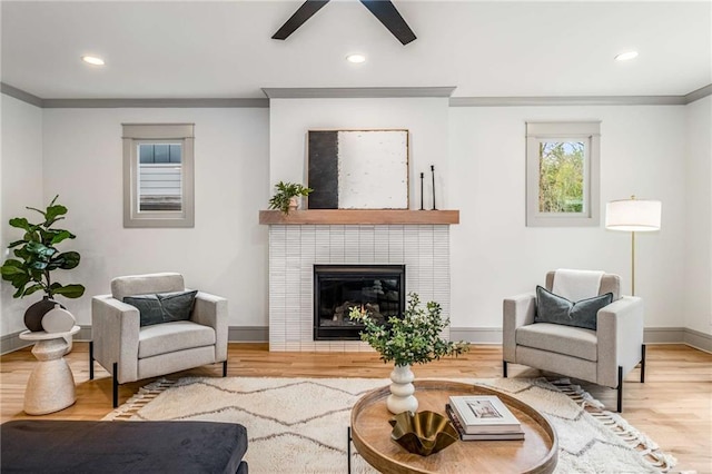 living area featuring a tile fireplace, recessed lighting, wood finished floors, baseboards, and ornamental molding