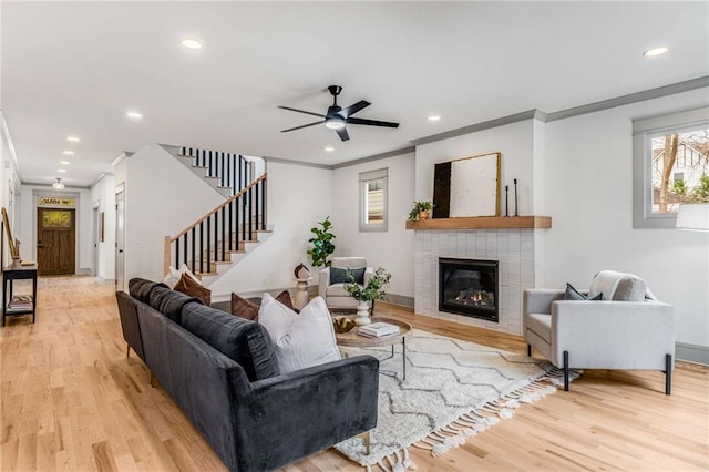 living room with stairs, recessed lighting, a tiled fireplace, and light wood-style floors