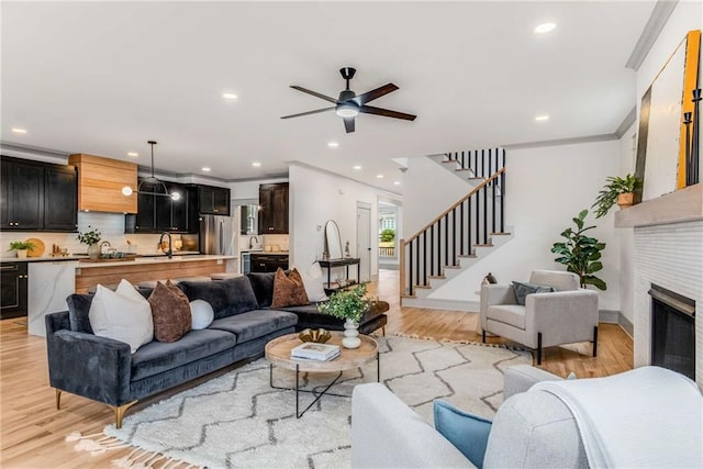 living area featuring recessed lighting, a fireplace, stairway, light wood-type flooring, and crown molding