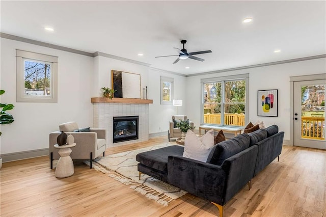 living room featuring light wood-type flooring, baseboards, ornamental molding, and a tiled fireplace