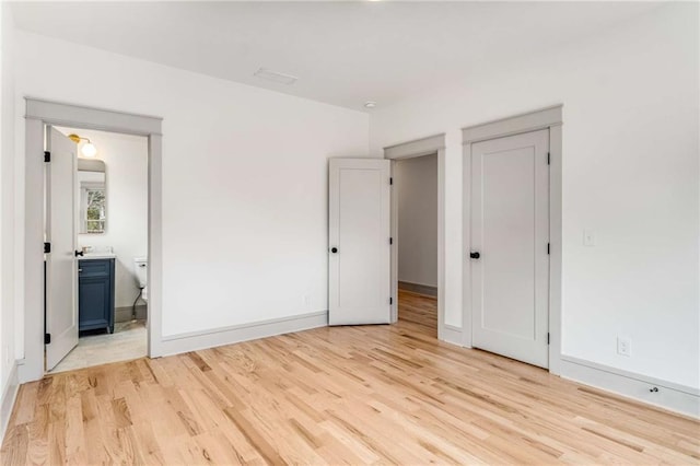 unfurnished bedroom with light wood-style floors, connected bathroom, and baseboards