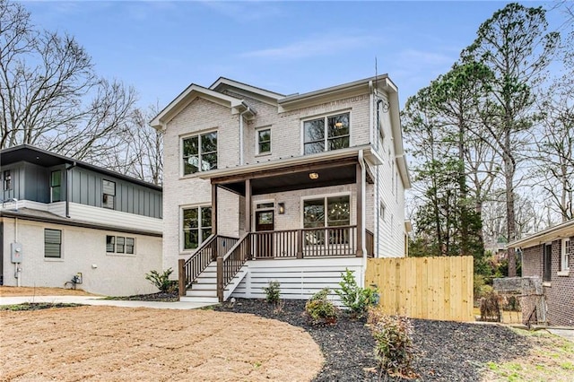 view of front of property featuring covered porch, brick siding, and fence