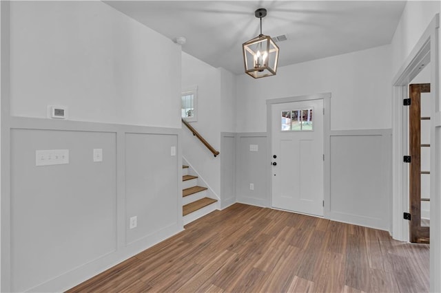 foyer entrance with stairway, a notable chandelier, wood finished floors, and wainscoting