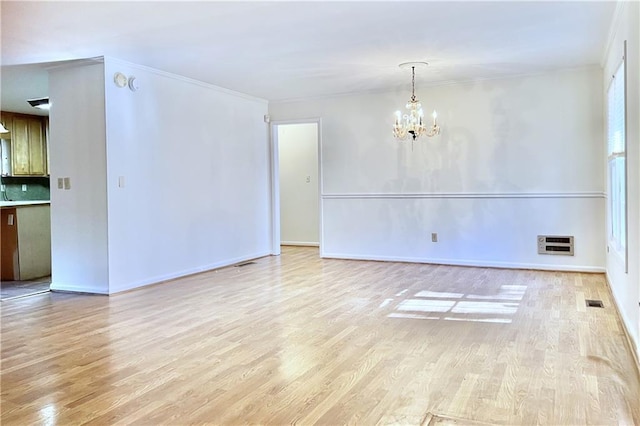 spare room featuring light hardwood / wood-style flooring, ornamental molding, and a chandelier