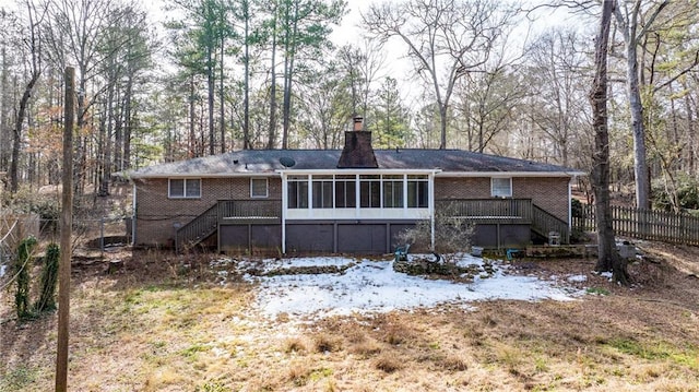 snow covered back of property featuring a wooden deck and a sunroom