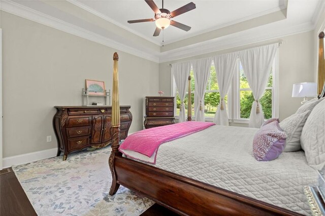 bedroom with crown molding, baseboards, ceiling fan, a tray ceiling, and light wood finished floors